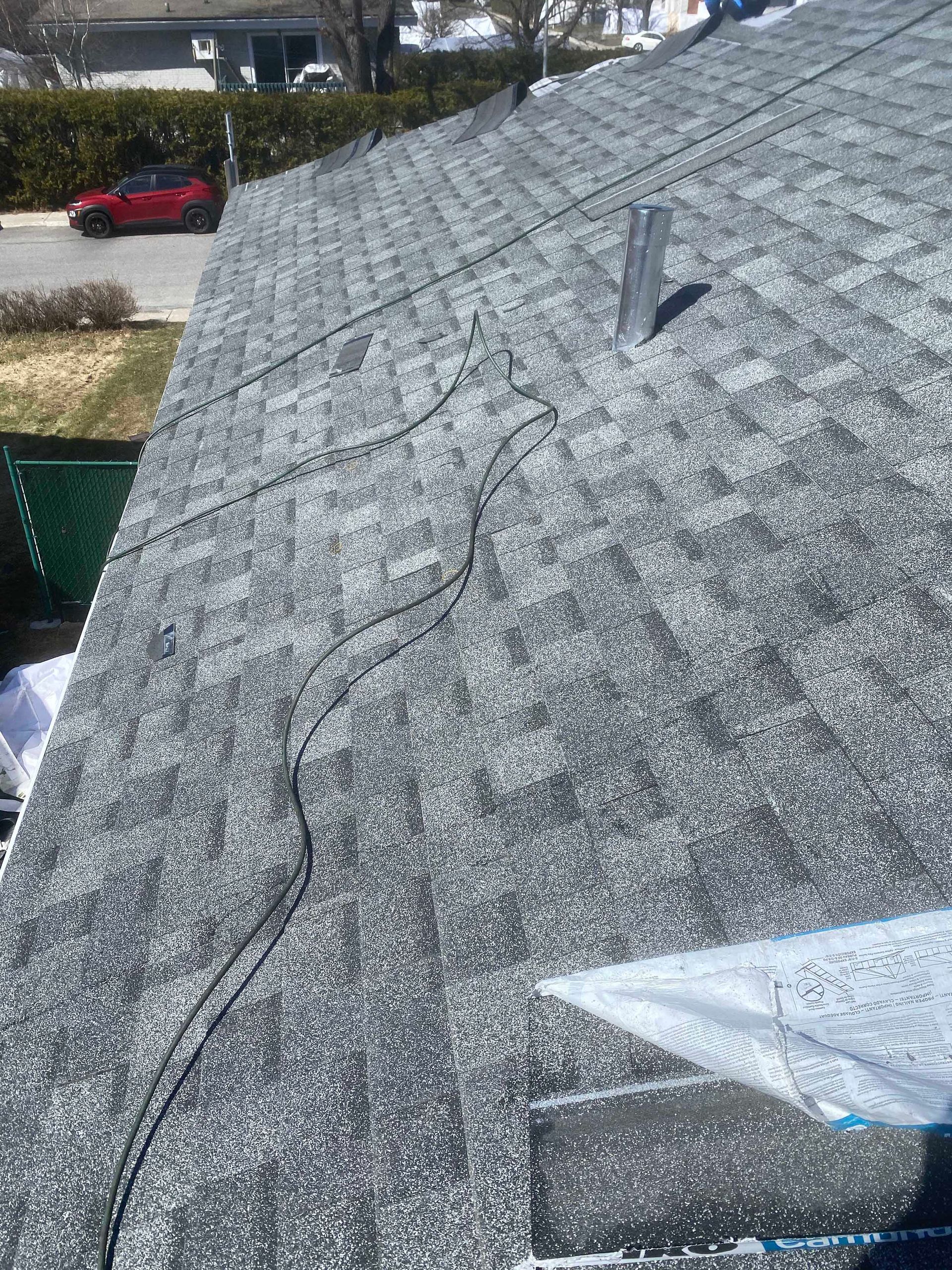 Vue d'un toit en bardeaux en construction, avec un fil électrique serpentant à sa surface.