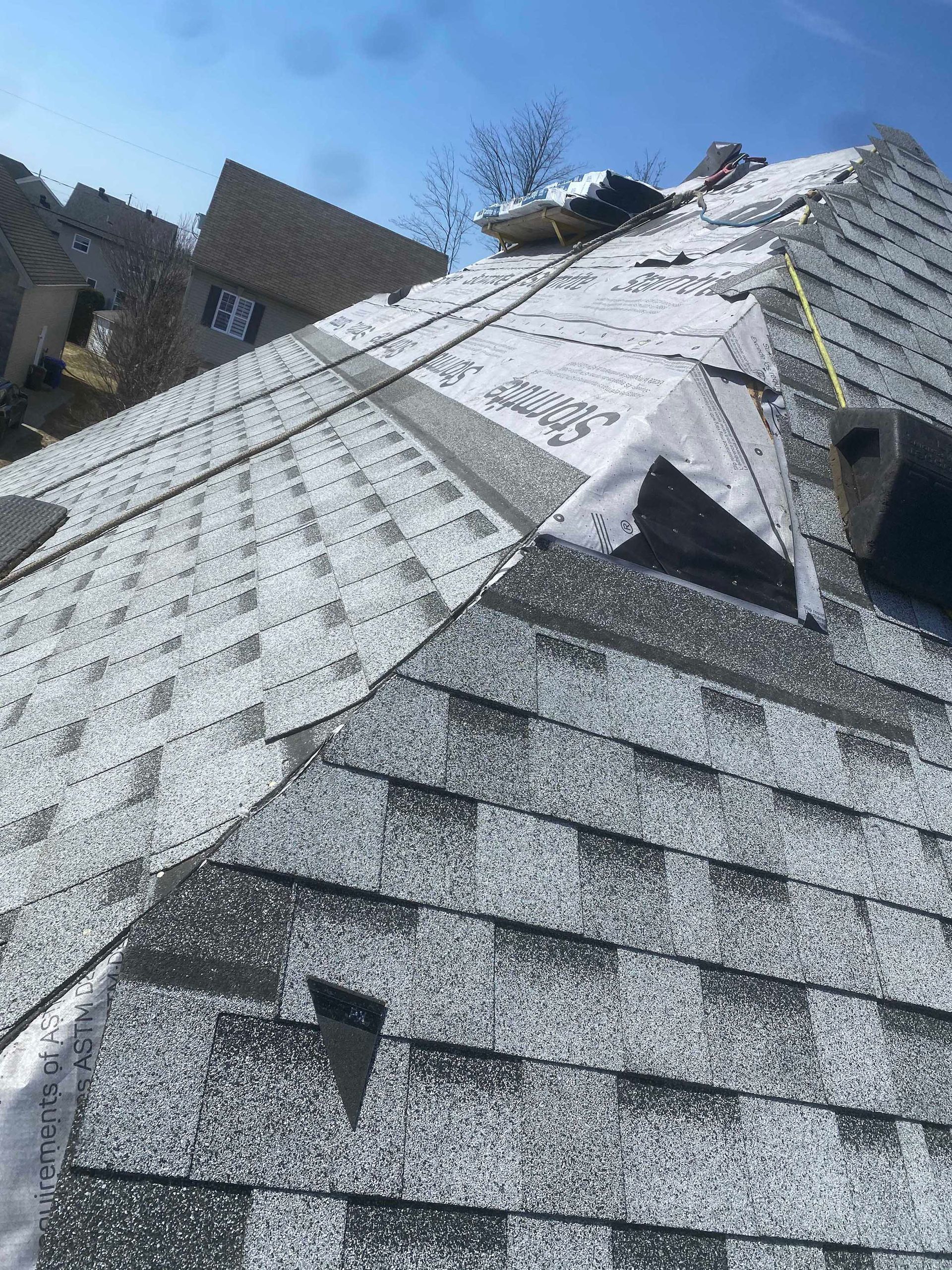 Un toit résidentiel à forte pente en construction, avec des bardeaux d'asphalte gris et une sous-couche synthétique blanche visibles.