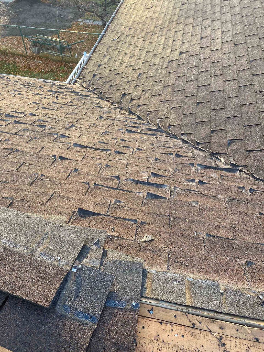 Close-up of a shingled roof with weathered brown and gray tiles and a ridge seam.