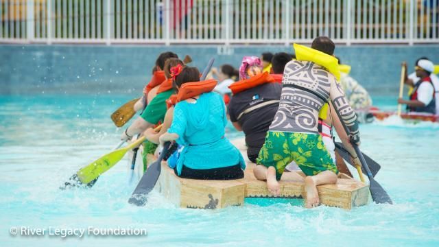 People in life jackets rowing a raft on turquoise water, viewed from behind