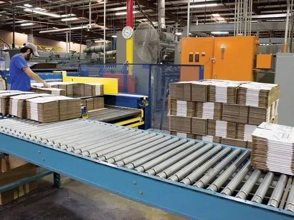 Factory conveyor with stacked cardboard boxes and a worker in a blue shirt