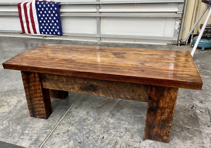 A wooden bench is sitting in front of an american flag.