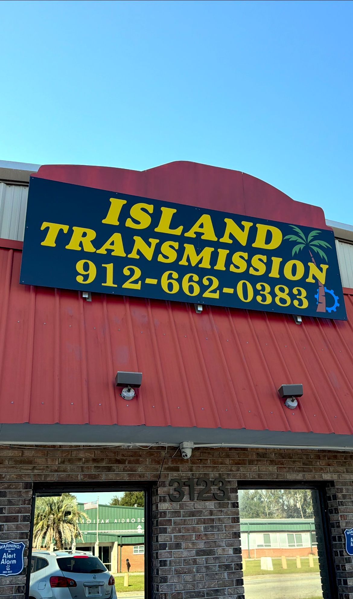 Sign for Island Transmission; yellow text on blue with a palm tree logo; phone number 912-662-0383; red roof.
