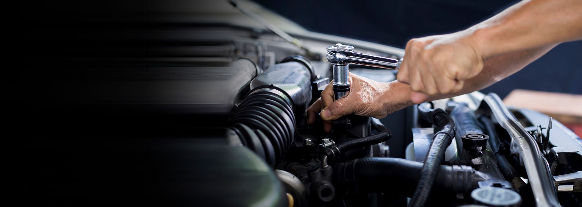 A person is working on the engine of a car with a wrench.