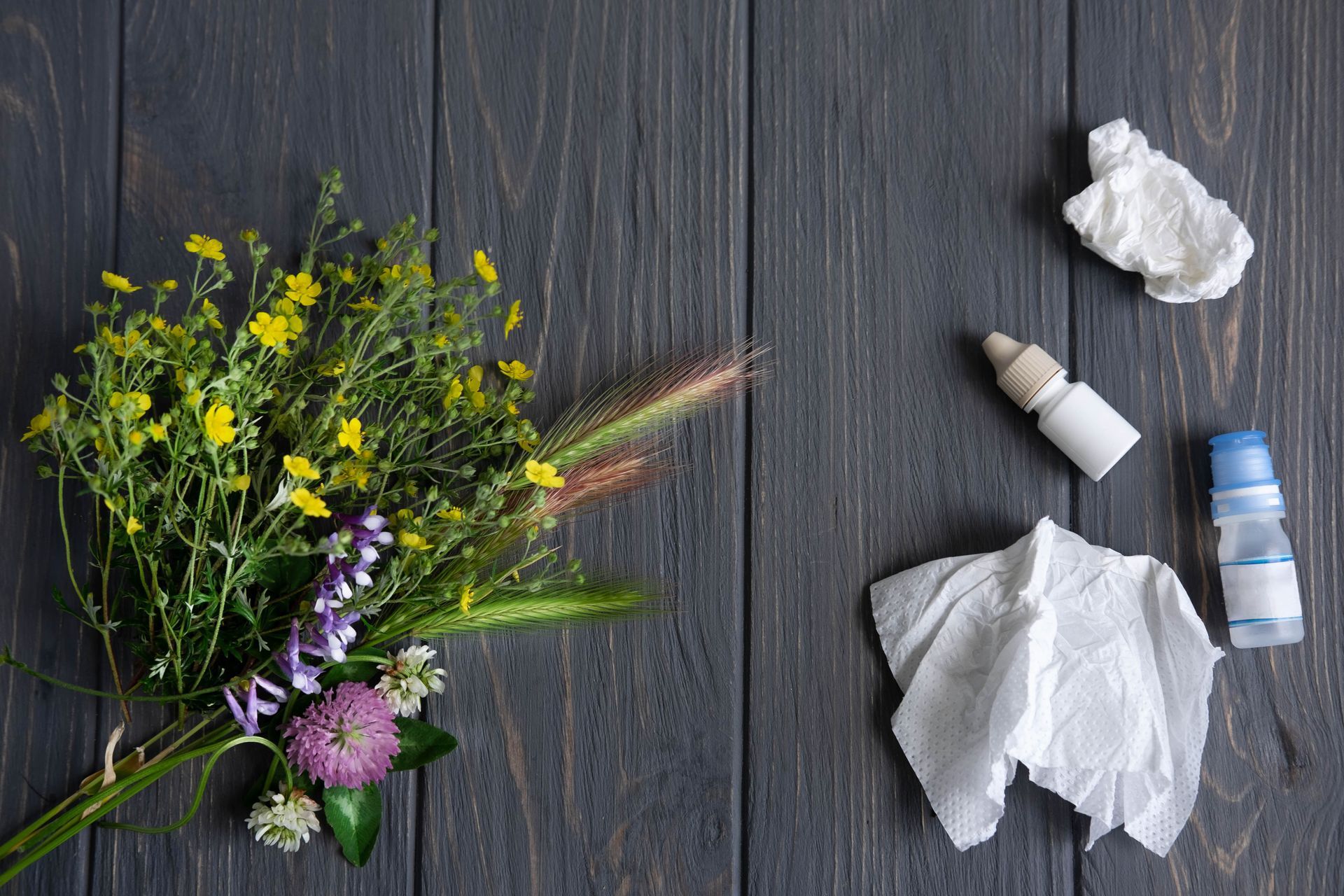 Flowers, a medicine bottle, and crumpled tissues on a dark wood table