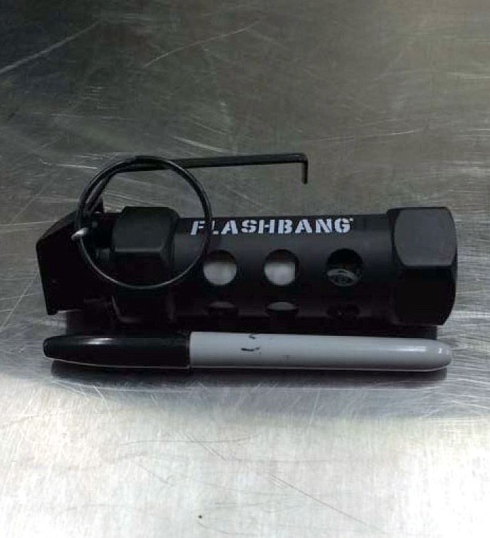 Black Flashbang device with attached cable, resting on a stainless steel surface beside a pen.