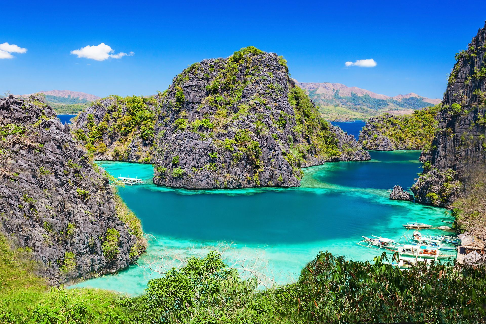 Turquoise tropical bay with rocky islands, clear water, and green hills under a blue sky