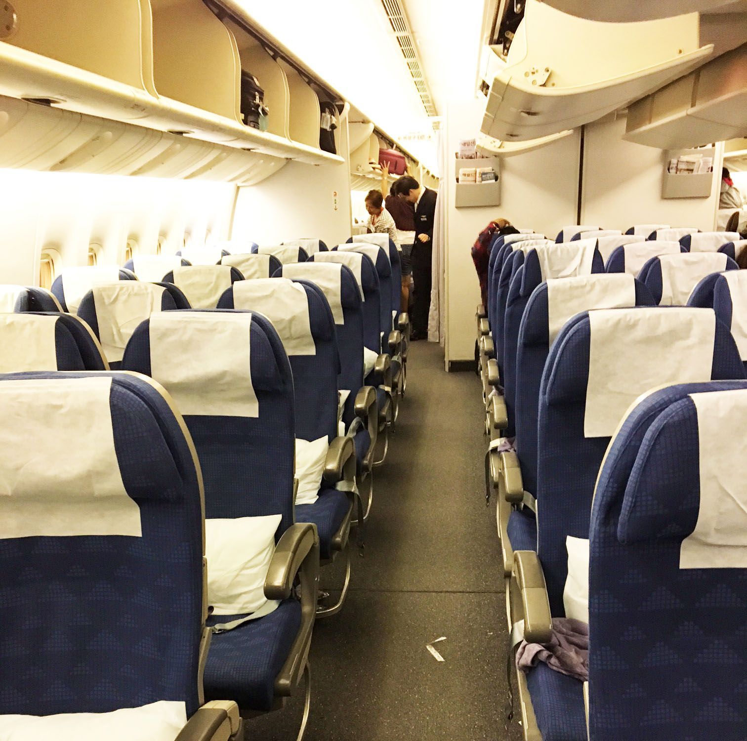 Airplane cabin with rows of blue-and-white seats and a few passengers near the front.