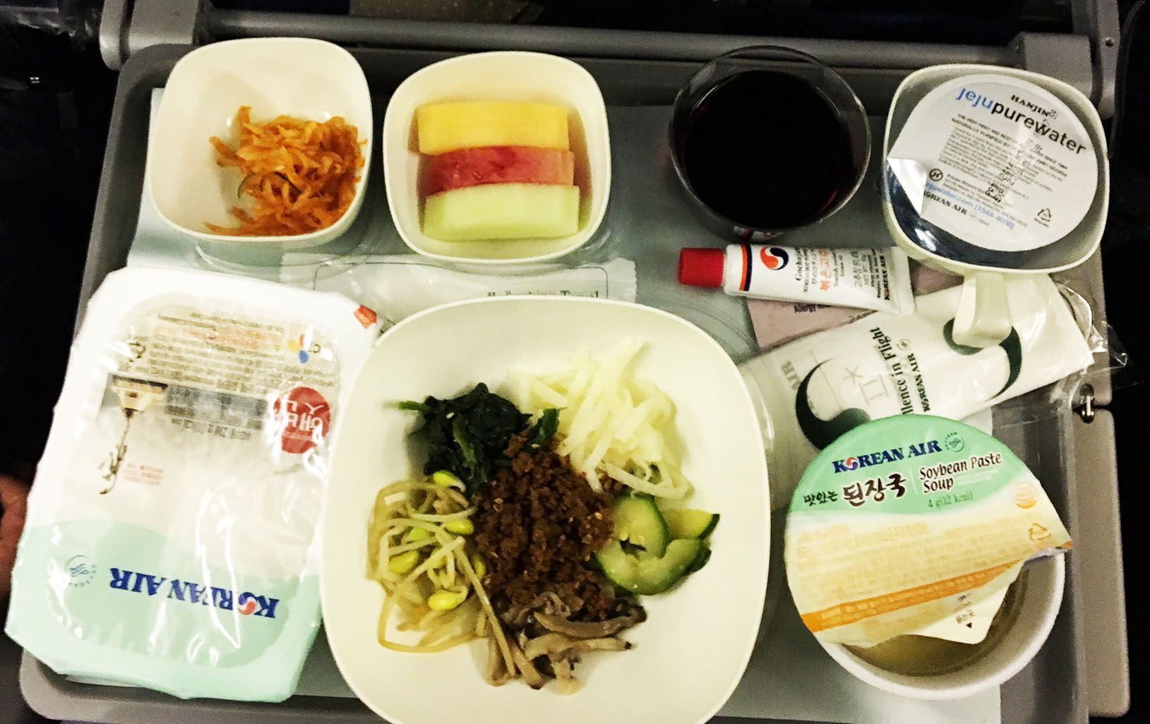 Tray with a meal, drinks, and packaged side dishes on an airplane tray table