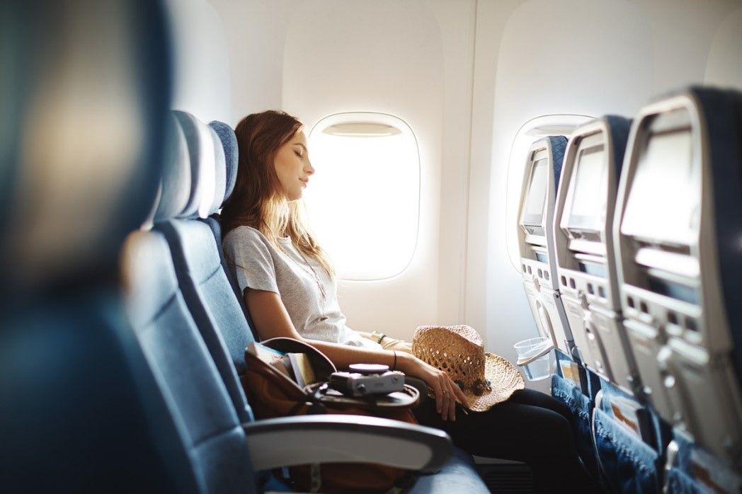 Passenger sitting by an airplane window with a tray table and seatback screens in front of her