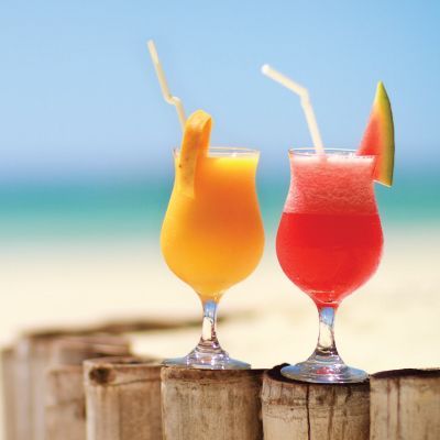 Two colorful cocktails with straws on a beachside wooden table, ocean in the background