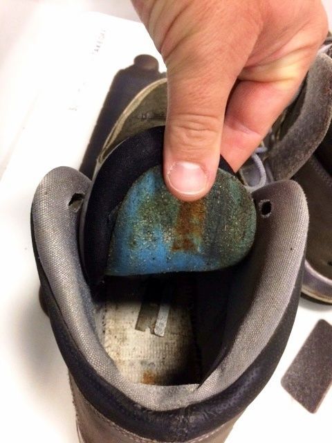 Hand holding up a worn blue shoe insole inside a black shoe