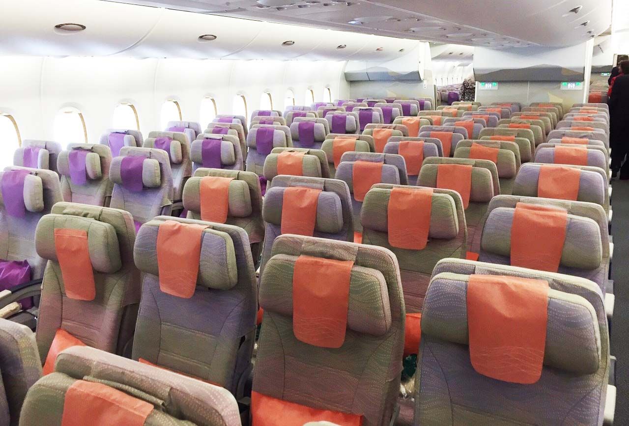 Empty airplane cabin with rows of gray seats and orange headrest covers, lit by overhead lights