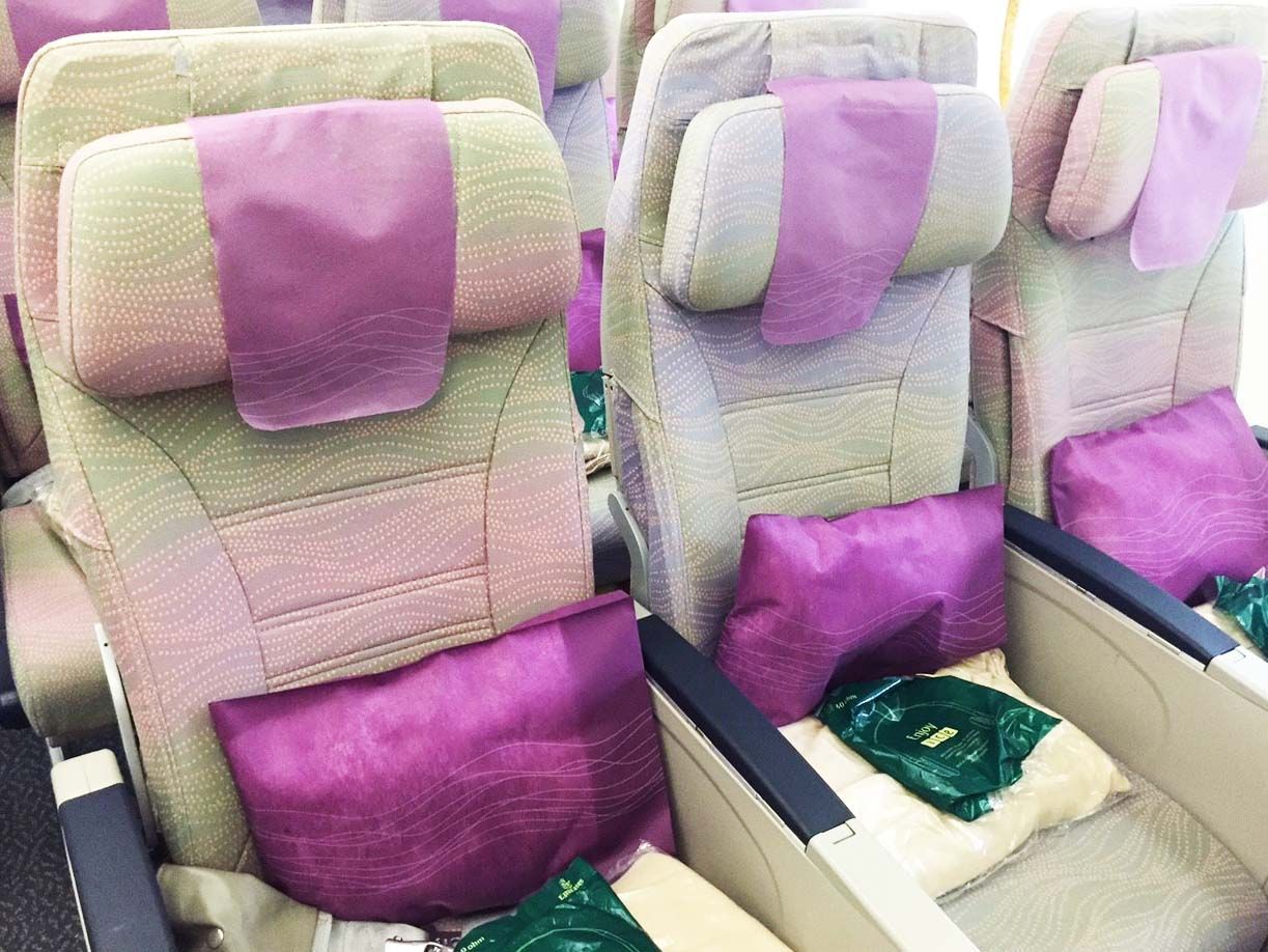 Row of airplane seats with purple and cream covers and purple pillows in a cabin.