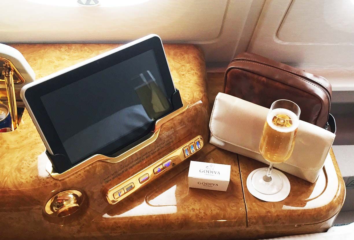 Tablet in a brown leather tray table with a drink and small items beside it on a plane seat