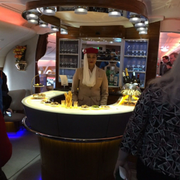 Person behind a lit bar counter in a modern lounge, with glass displays and bottles in the background.