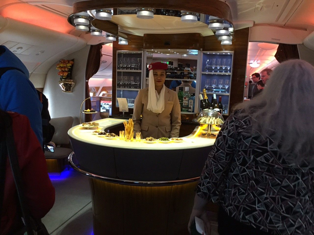 Bartender behind a glowing circular bar in a sleek lounge, with patrons seated nearby.