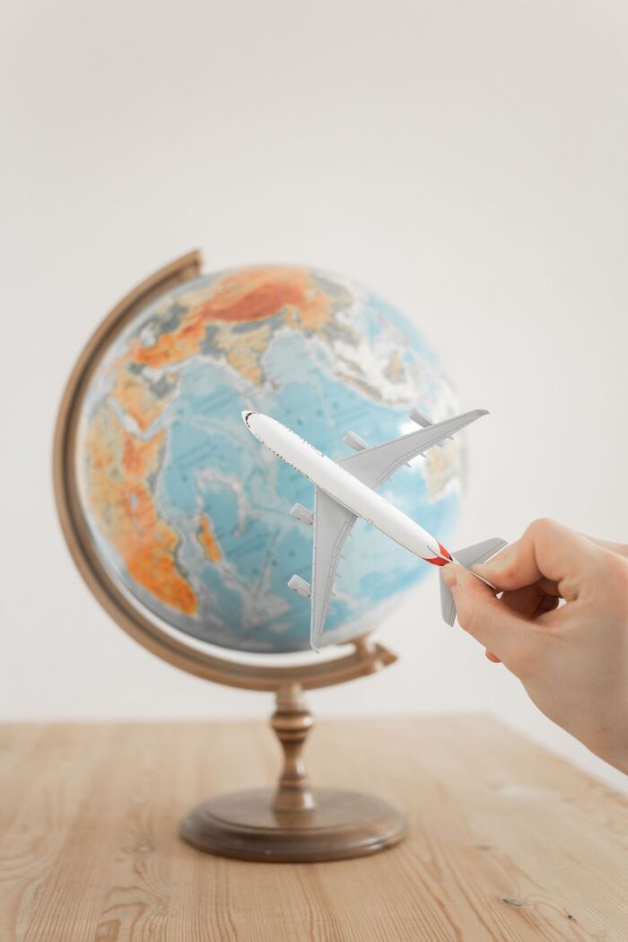 Hand holding a pen pointed at a globe on a wooden table