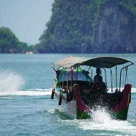 Long-tail boat speeding across blue water near rocky green islands.