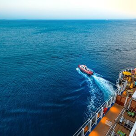 Small boat speeding beside a cruise ship at sea, leaving a white wake