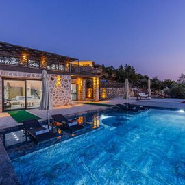 Modern villa with lit patio beside a glowing blue infinity pool at dusk