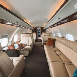 Private jet cabin with beige leather seats, windows, and overhead compartments