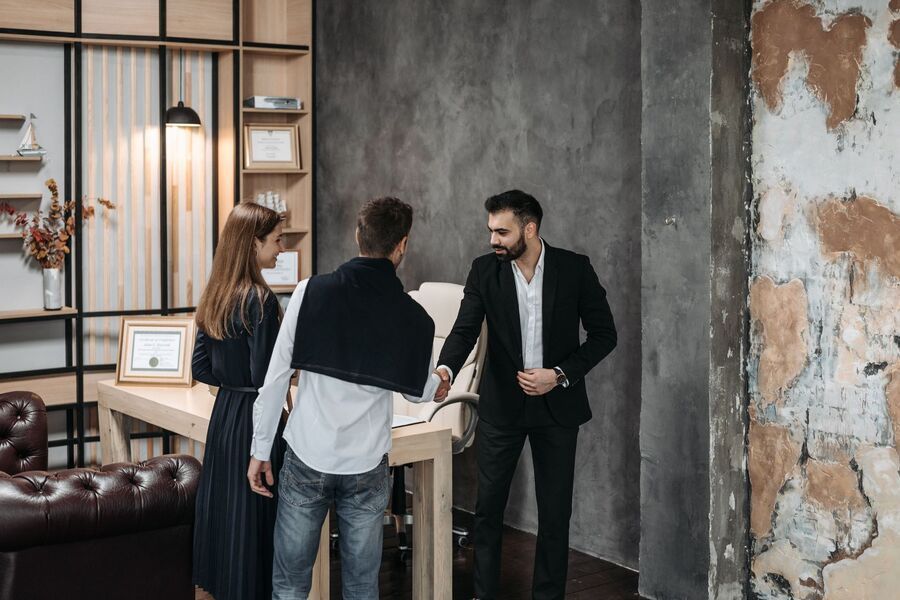 Three people talking beside a table in a modern lounge with a leather sofa and concrete wall.