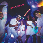 People dancing at a neon-lit party under a disco ball, wearing white outfits and smiling