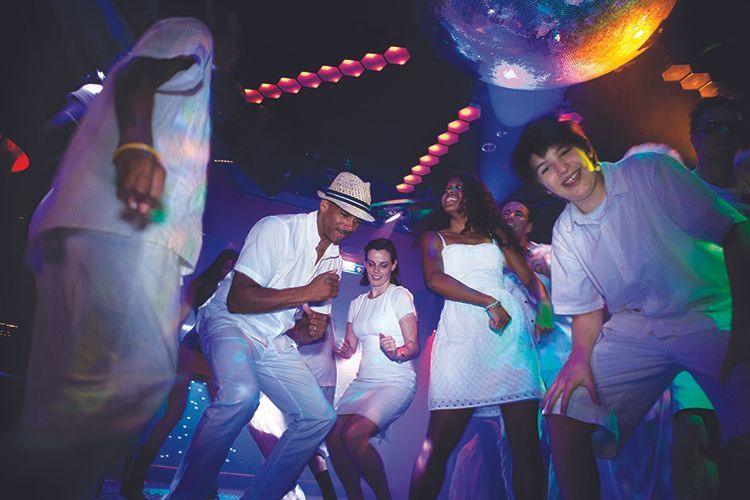 People dancing at a neon-lit party with colorful lights and a disco ball overhead