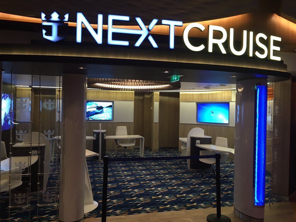 NEXTCRUISE booth entrance with glowing sign, blue lighting, and lounge chairs inside a cruise exhibition space