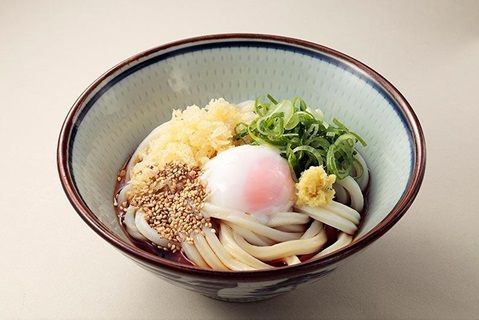 Bowl of udon noodles topped with a soft-boiled egg, tempura crumbs, and green onions