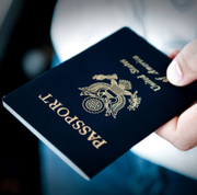 Hand holding a blue passport with gold emblem and “PASSPORT” text