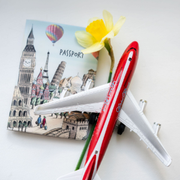 Travel-themed passport with a red toy airplane, yellow flower, and landmark postcard.