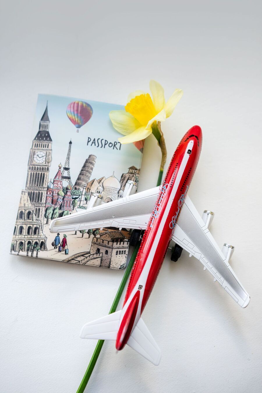 Toy airplane and red pen crossed over a small notepad with a yellow flower on a white background