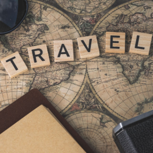 Vintage travel-themed flat lay with “TRAVEL” letter tiles on an old map, camera, notebook, and glasses