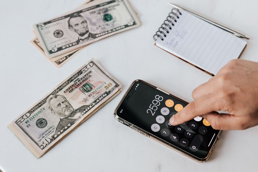 Hand using calculator beside cash and notebook on a white desk
