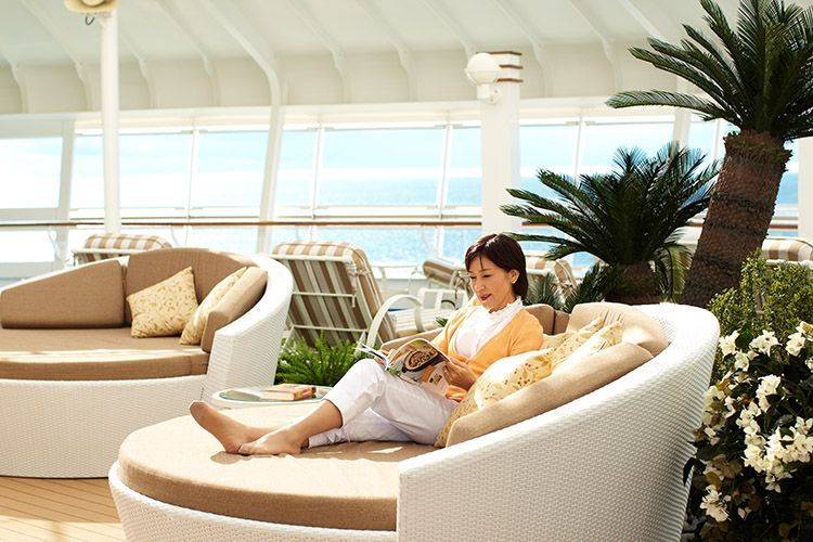 Person relaxing on a white chaise lounge in a bright lounge area with large windows and palm plants