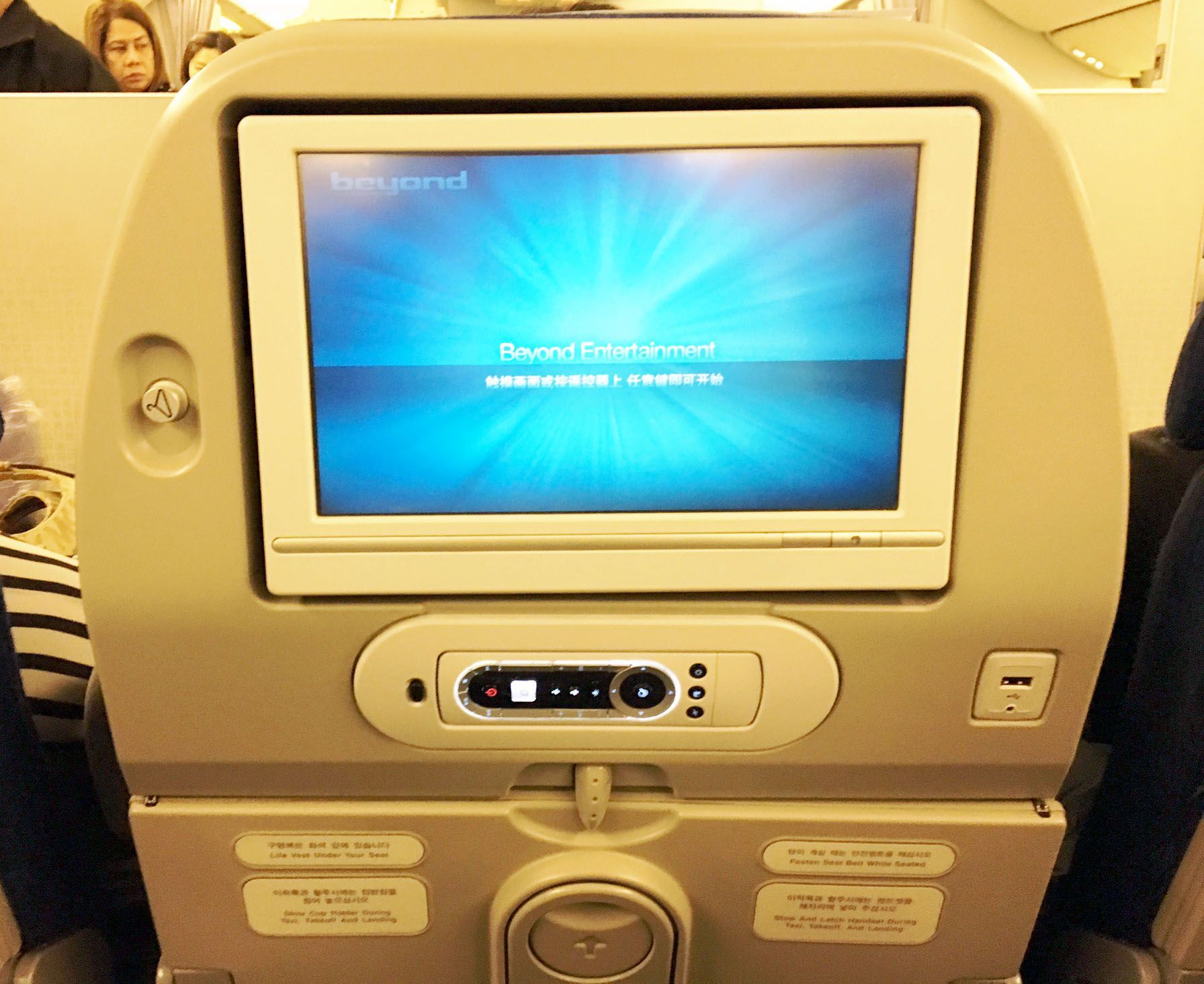 Airplane seatback entertainment screen with blue welcome display and control panel below