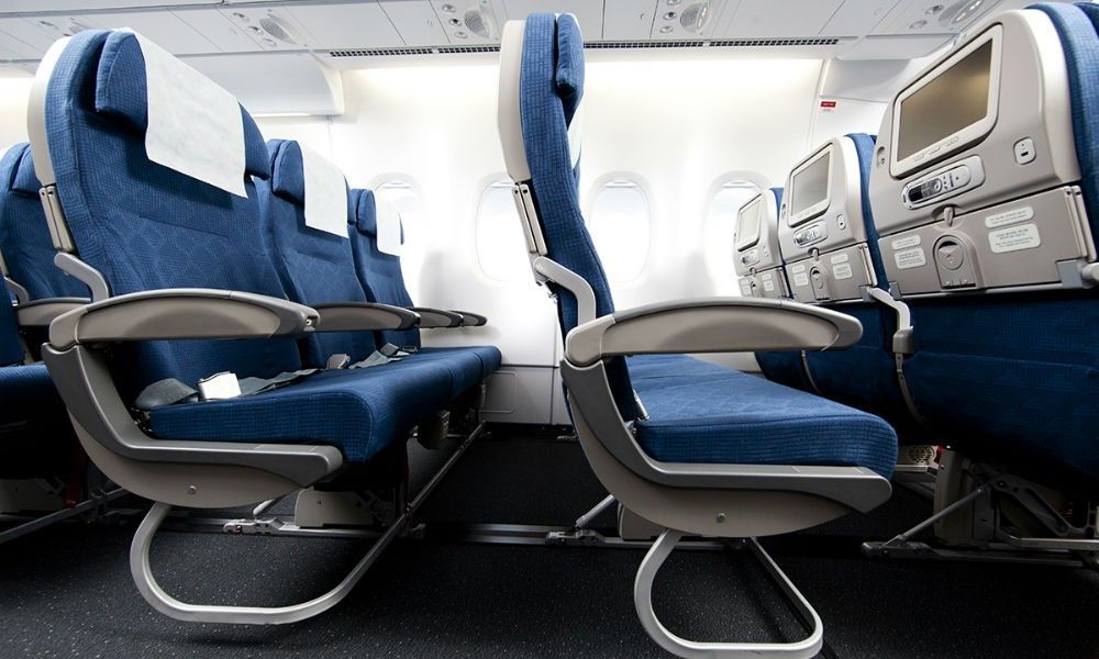 Blue economy-class airplane seats in a cabin interior with tray tables and overhead bins