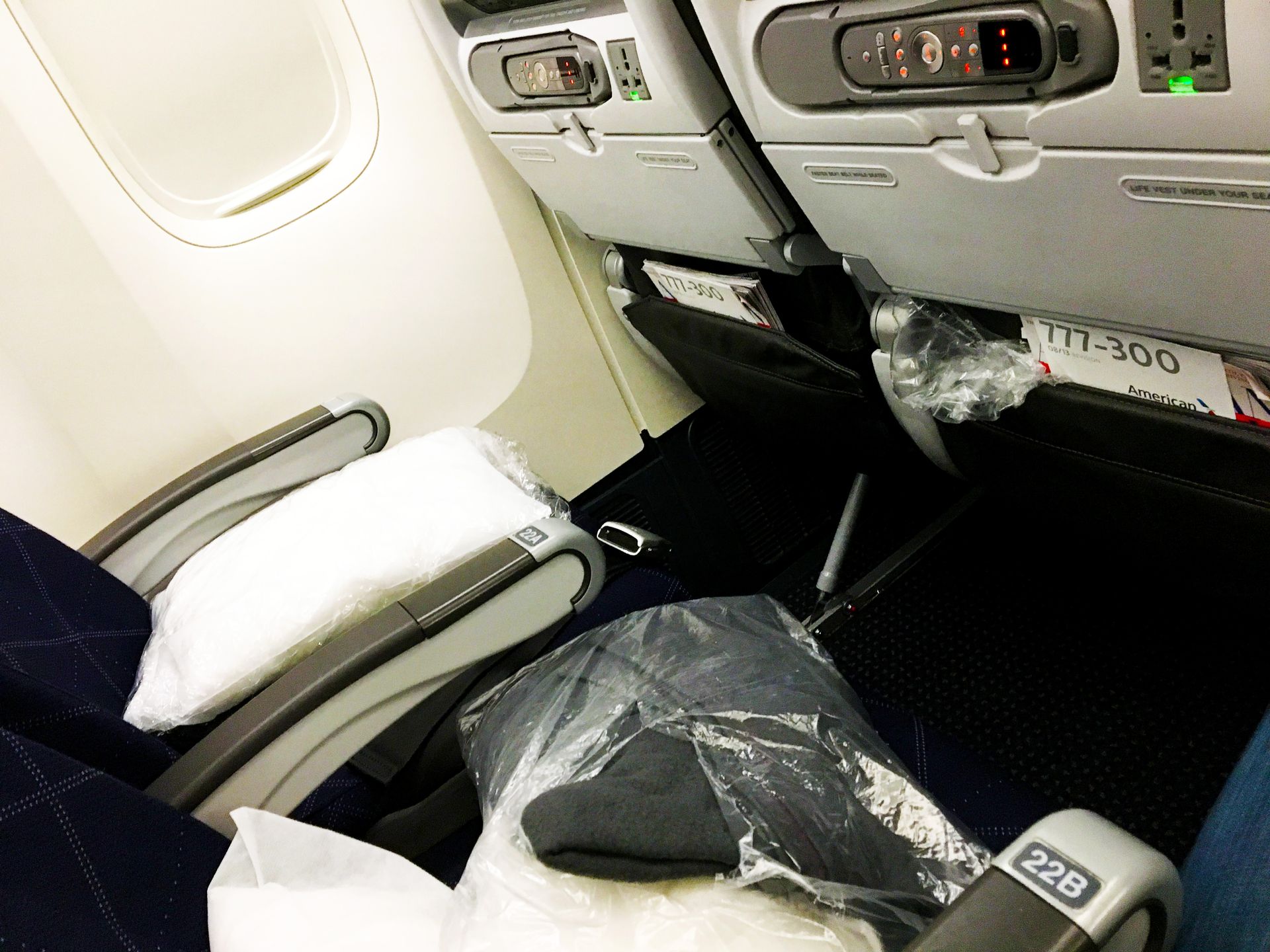 Airplane seat with tray table, armrests, and plastic-covered items, viewed from the aisle