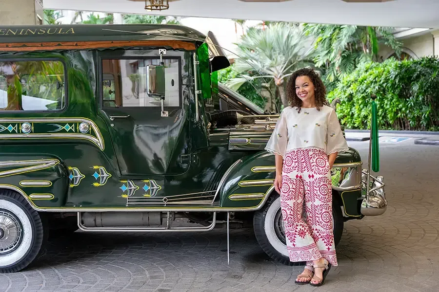 Woman standing beside a green vintage jeep in a lush tropical setting