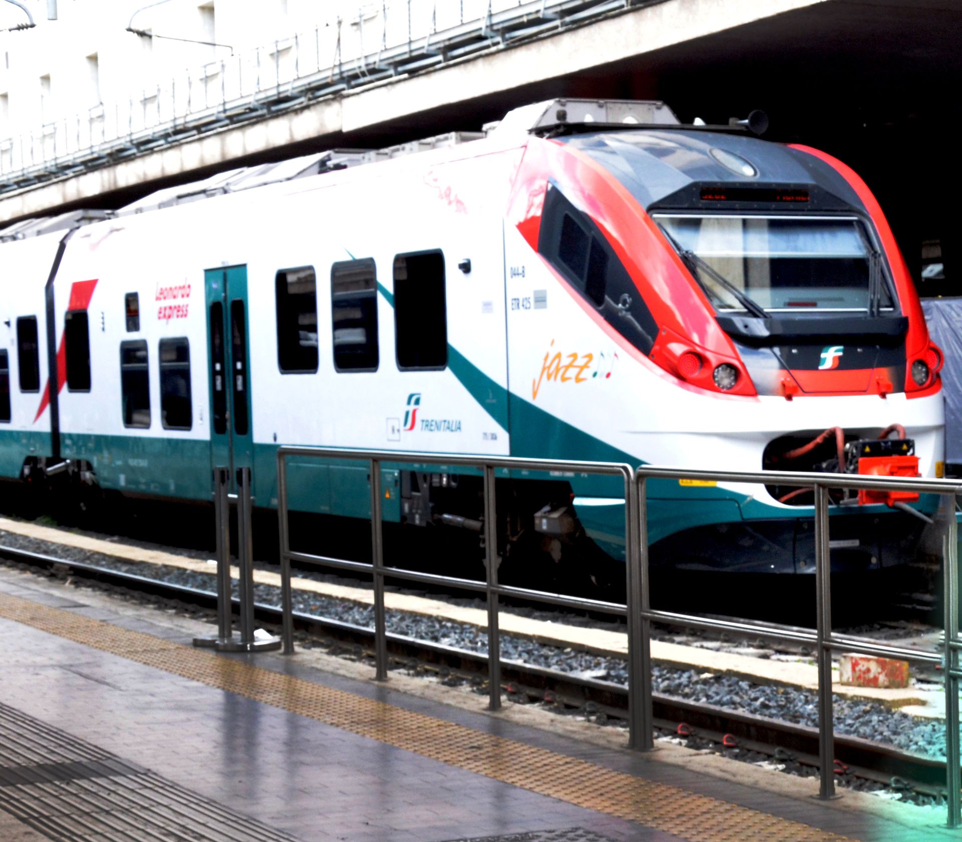 Red-and-white modern train at a station platform with railings and overhead structure