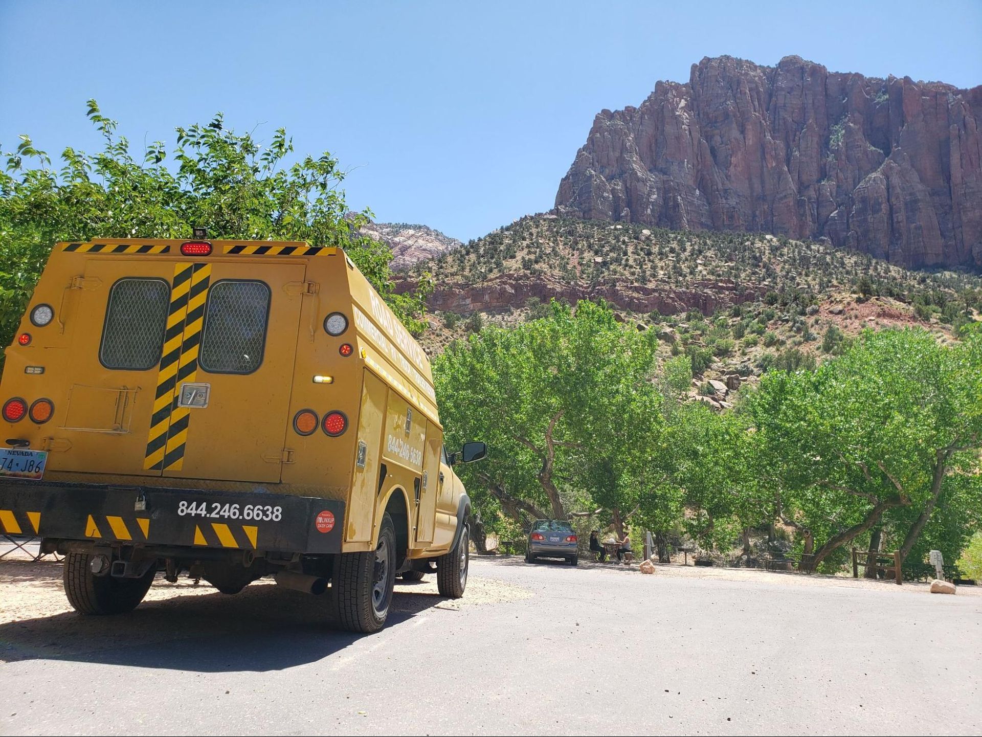A yellow truck with a mountain in the background is parked on the side of the road