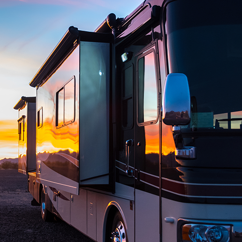 A large rv is parked in front of a sunset.