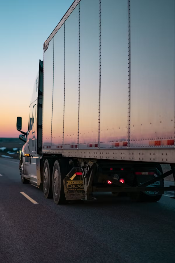Semi-truck driving on a highway at sunset, seen from the rear side.