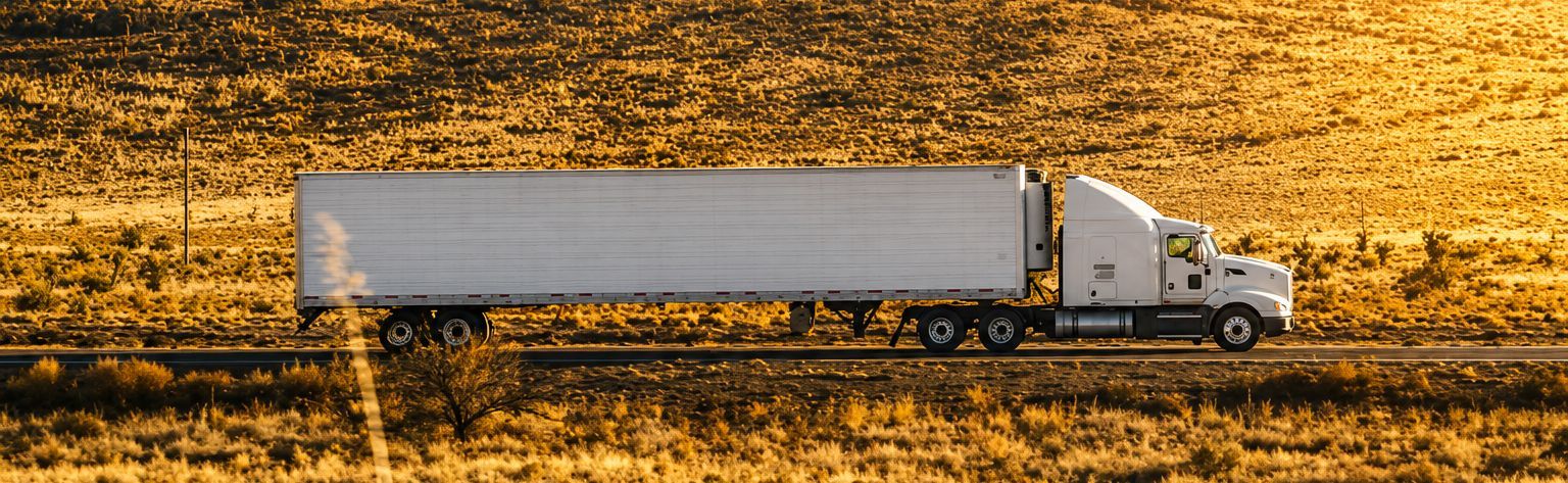White semi-truck hauling a trailer across a golden field at sunset