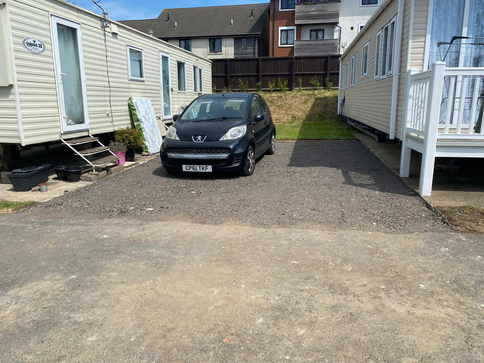 A black car parked on gravel in a caravan park, with caravans on either side.