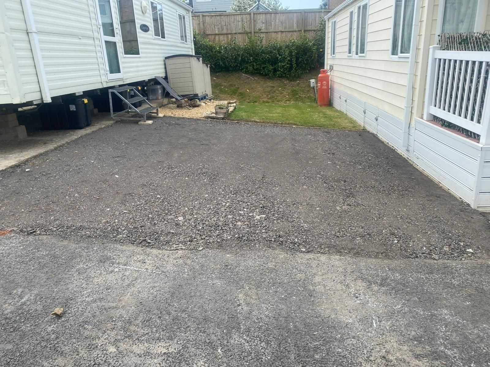Gravel-covered area between two buildings, possibly a driveway or parking spot.