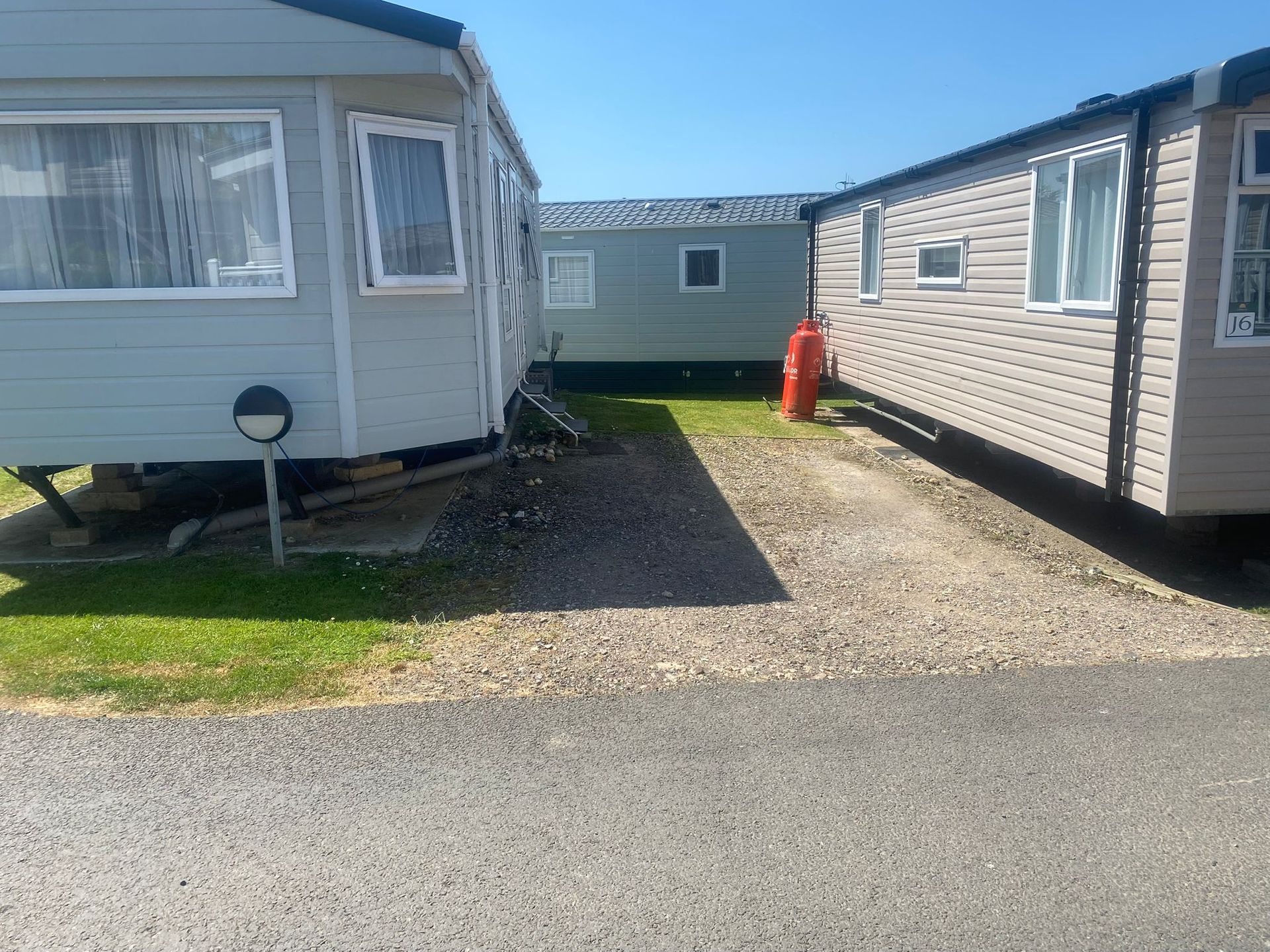 Caravans on a gravel drive in a sunny caravan park; grass, blue sky.