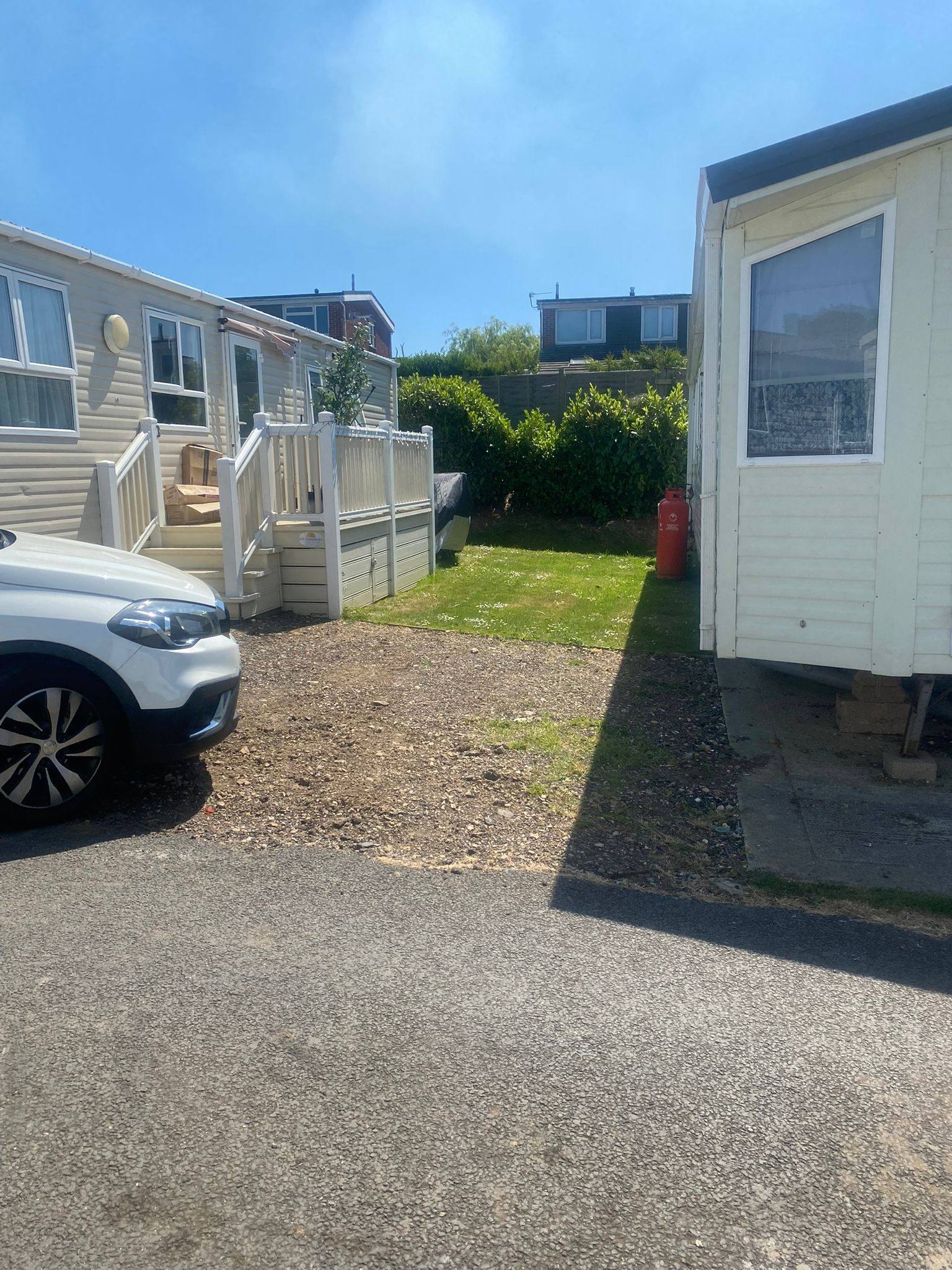 A white car parked next to two mobile homes. Gravel and grass in between. Sunny day.